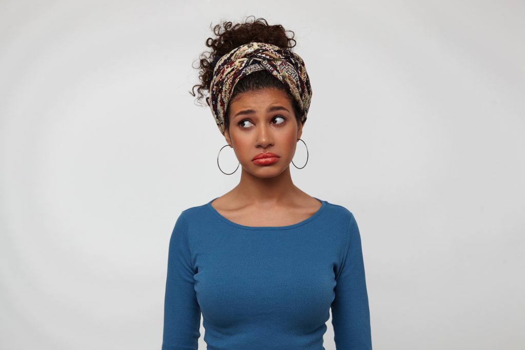 offended young lovely brunette dark skinned female twisting her mouth while looking sadly aside keeping hands along body while standing over white background 1024x683 1