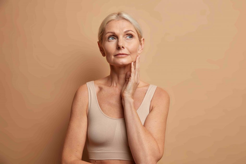 woman touches skin after applying anti age cream concentrated with thoughtful expression wears cropped top isolated brown 1 1024x683 1